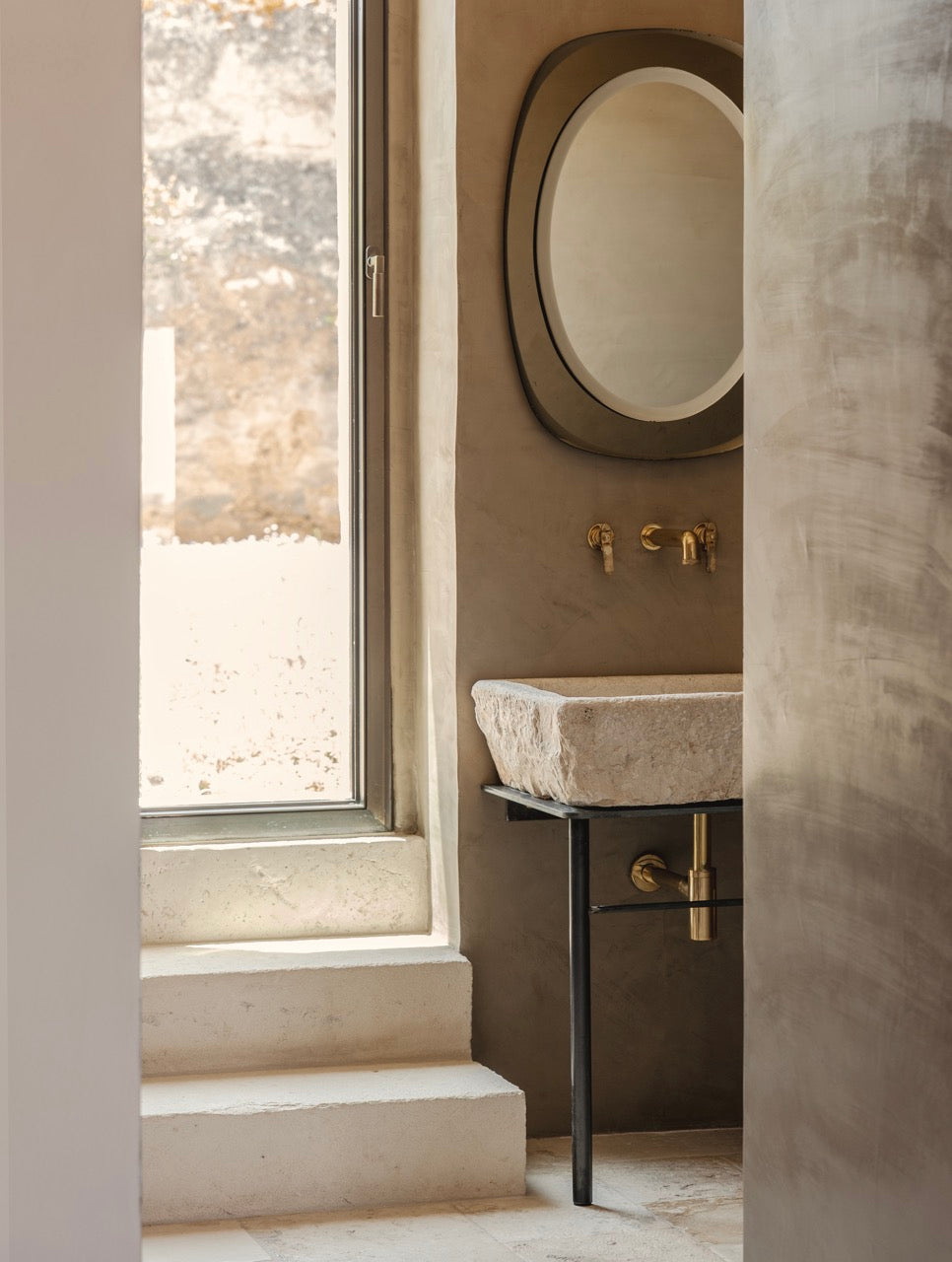 Bathroom vignette with carved stone sink, brass fixtures, and round mirror