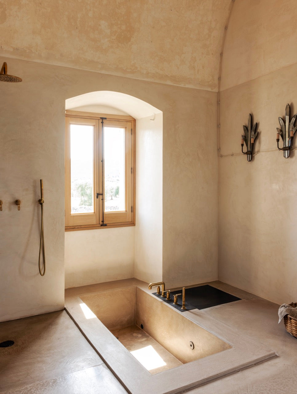 Sunken bathtub with brass fixtures and arched window in bathroom
