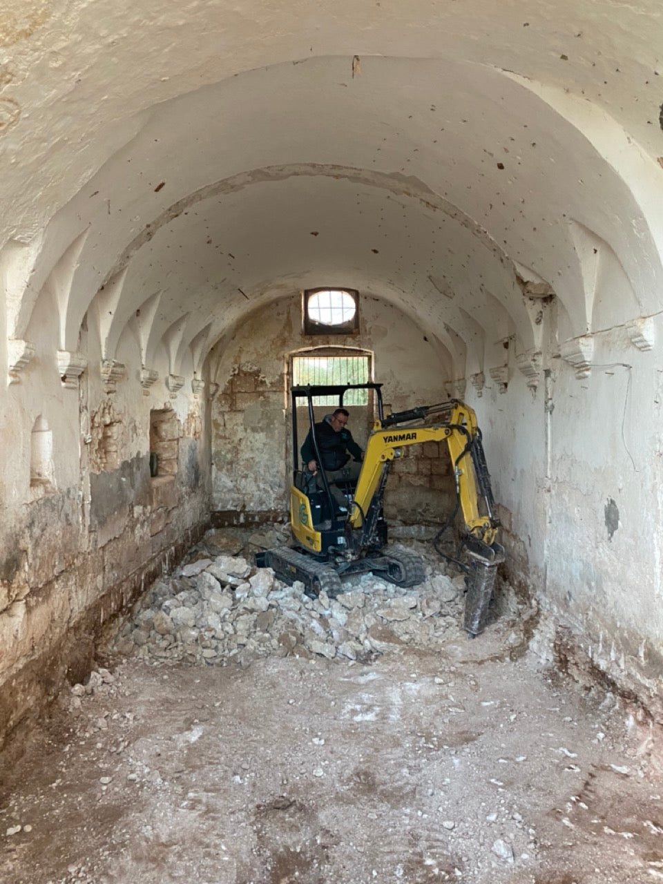 Yellow excavator digging up rubble in vaulted stone chamber