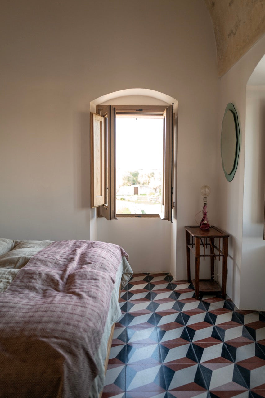 Bedroom corner with wooden side table, arched window and round mirror