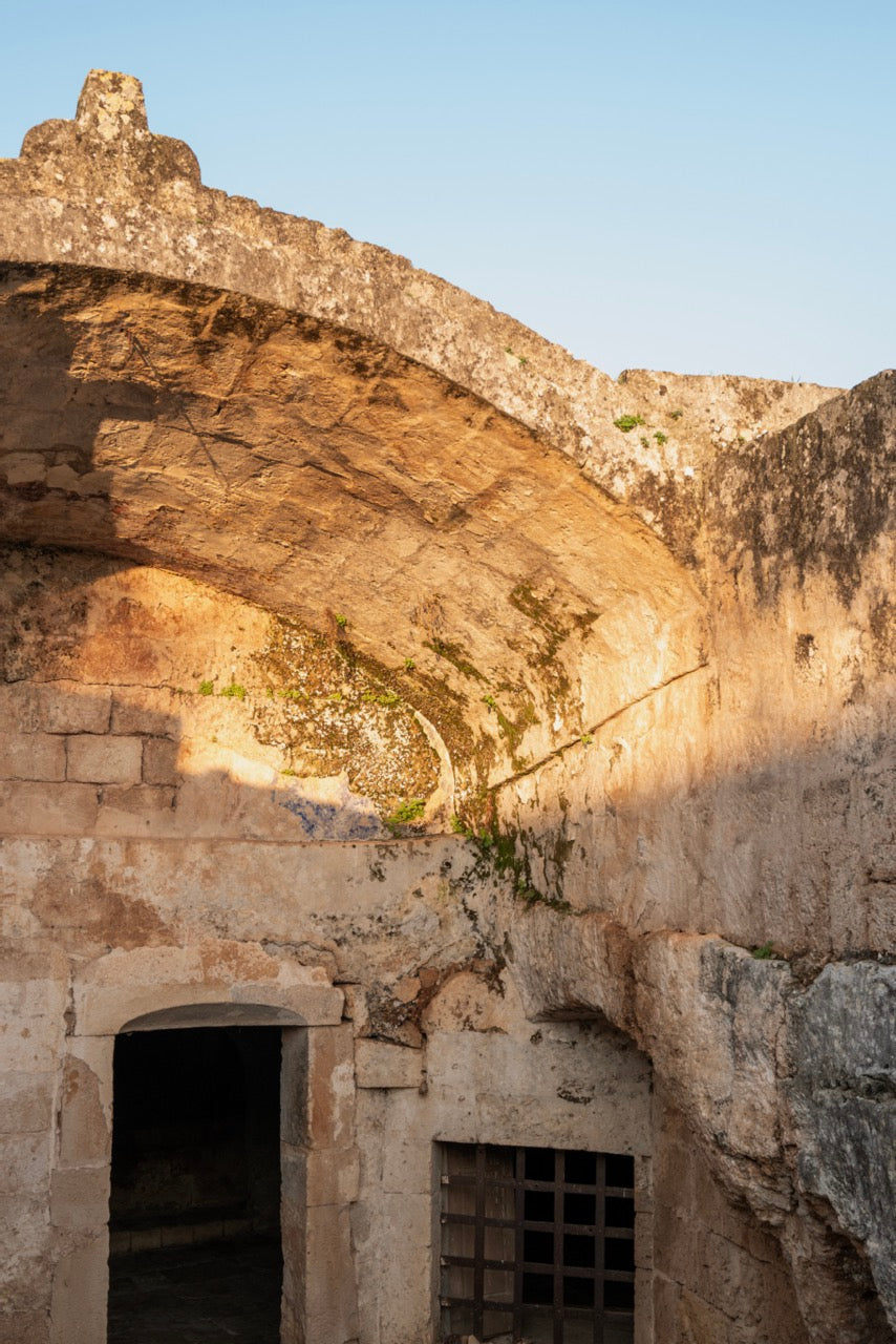Ancient stone grotto with archway and open space under a clear sky