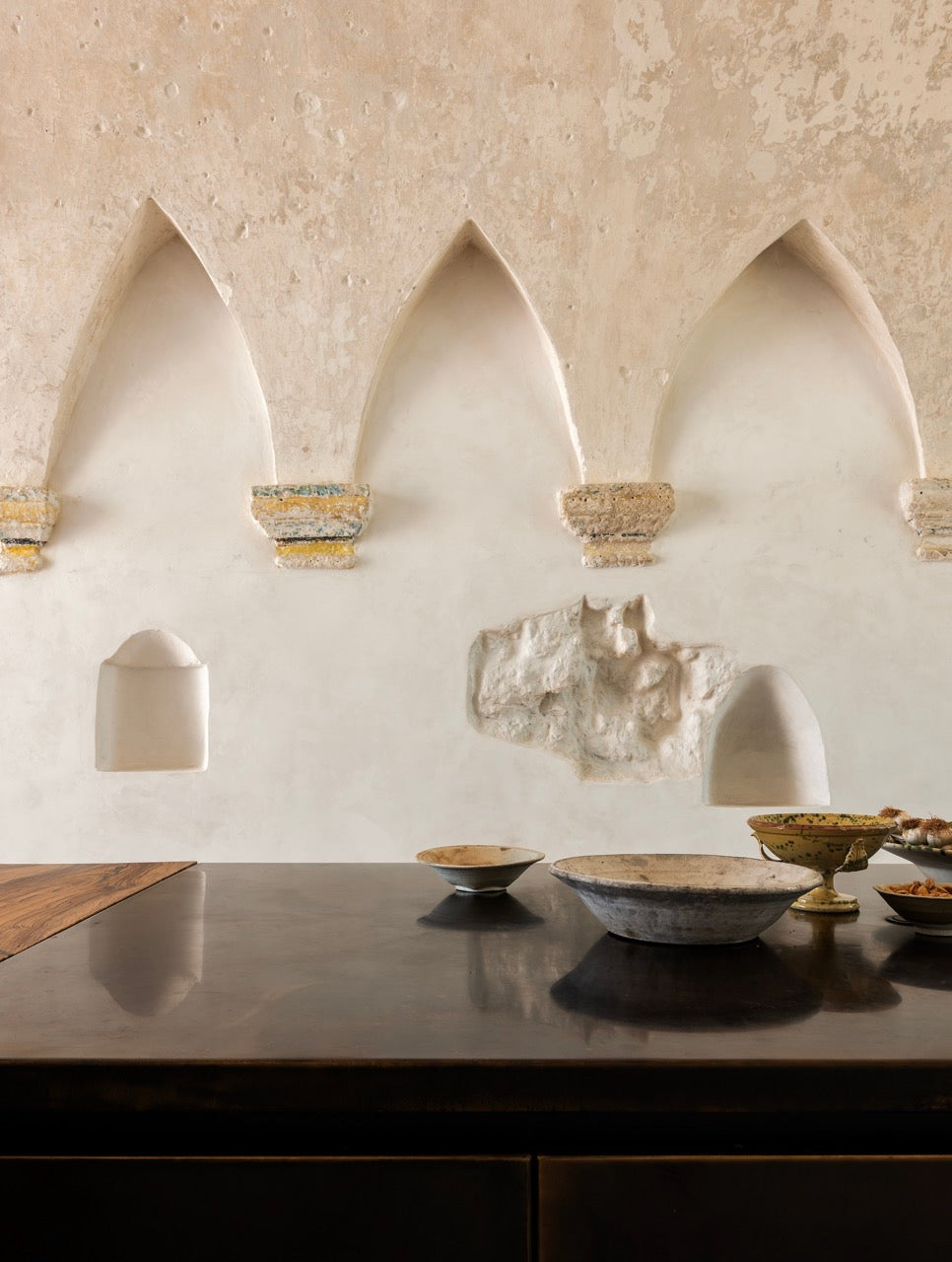 Arched wall niches above dark wood table with ceramic bowls