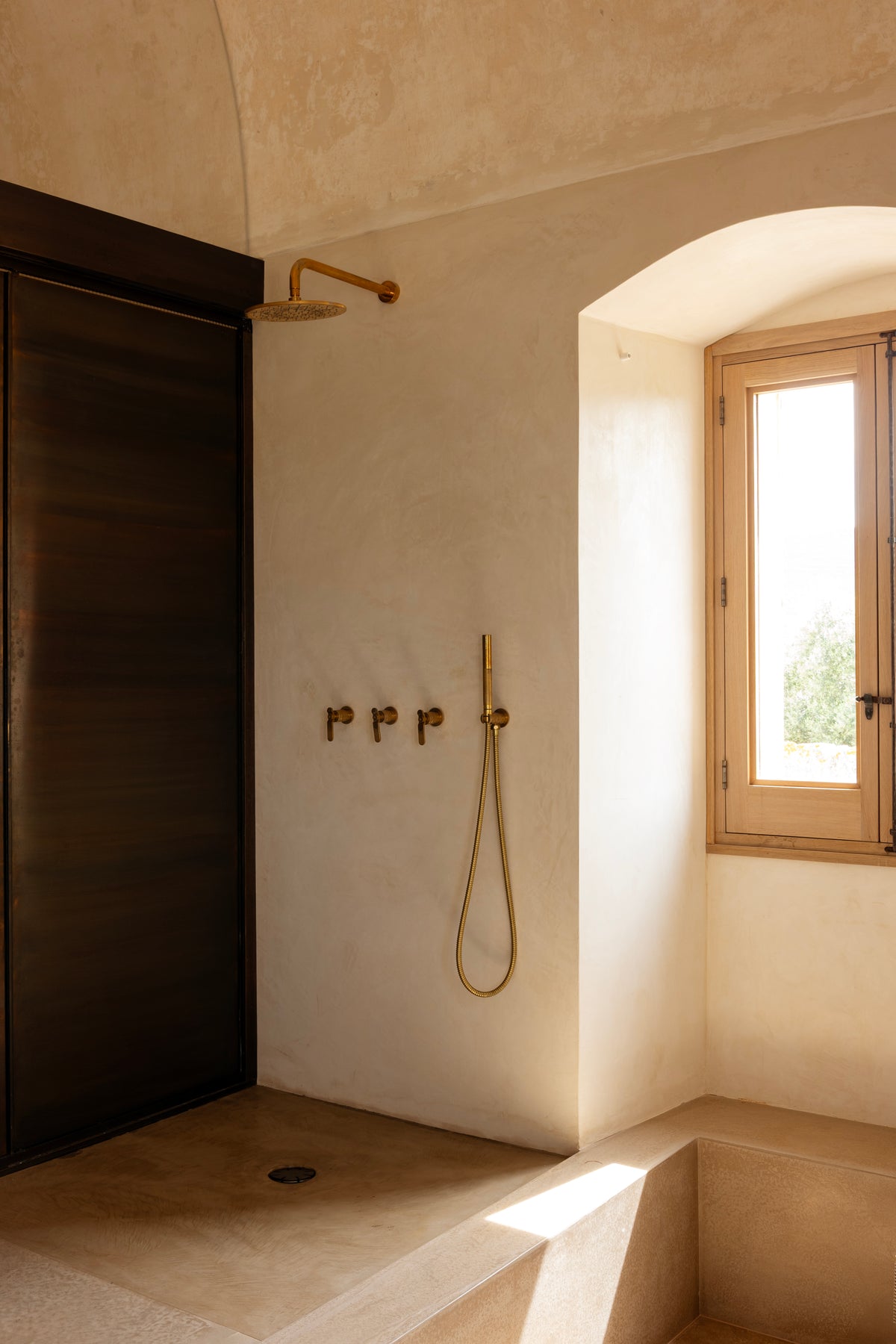 Open stone shower with brass fixtures and arched window