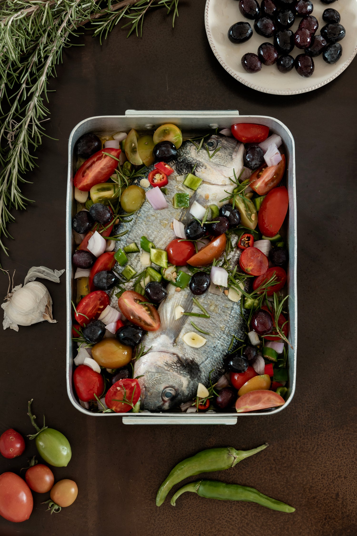 Whole fish in roasting tray with tomatoes, olives, and rosemary