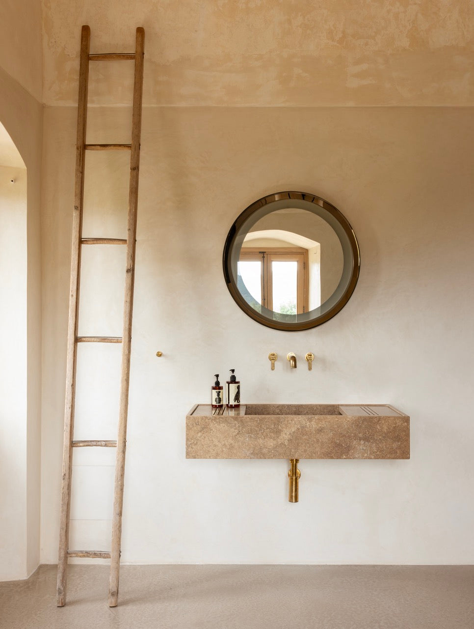 Stone bathroom sink with round mirror and brass fixtures