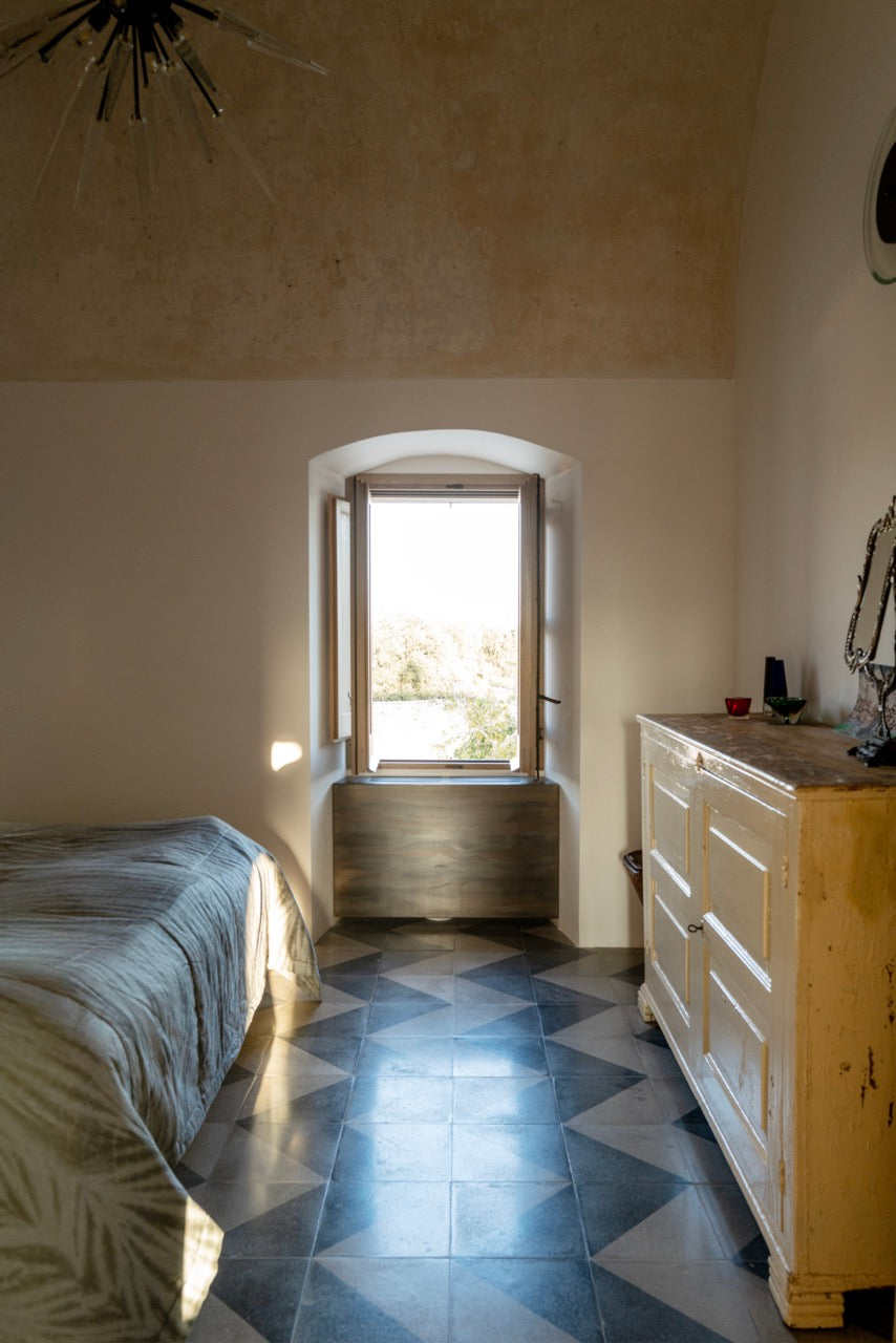 Bedroom with arched window, geometric tile floor, and antique dresser