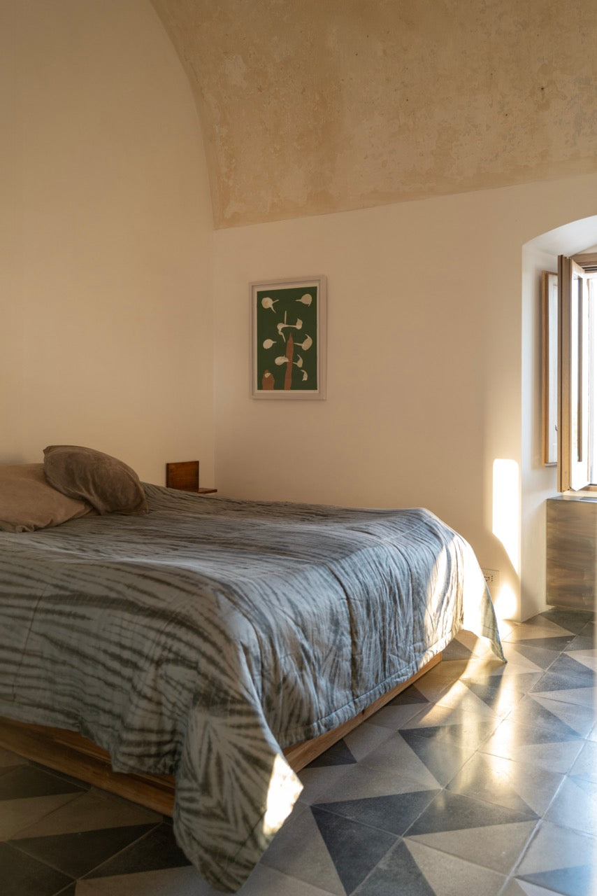 Vaulted bedroom with patterned linen bedding and green framed artwork